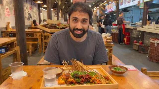 Beat 1: wide shot, the man at a food hall table with skewers on a tray.
