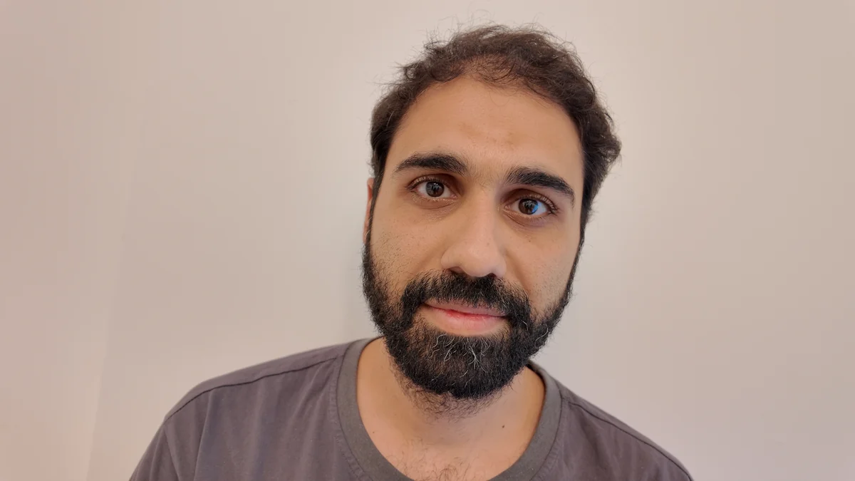 Front photo: the man faces the camera with a neutral expression, grey t-shirt, plain light wall.