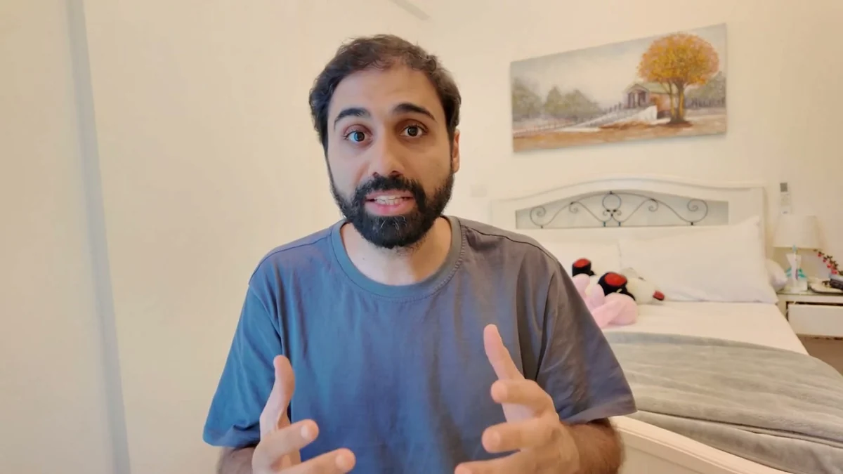 The Seedance clone of the same shot: the same room with the tree painting, the scrolled headboard, the plush toys and the nightstand, the man in the same blue t-shirt.