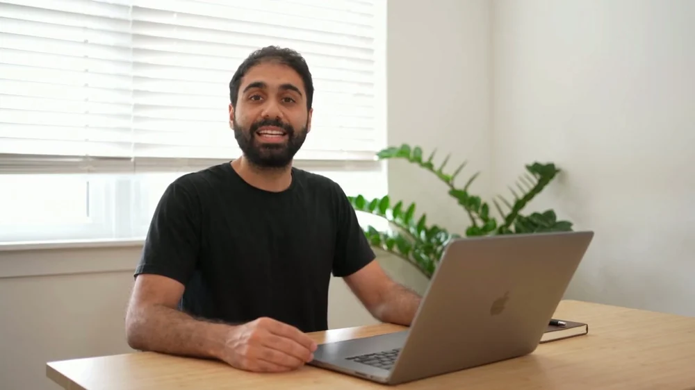 A Seedance render of the man in a black t-shirt at a desk by a window, smiling widely with an open mouth.